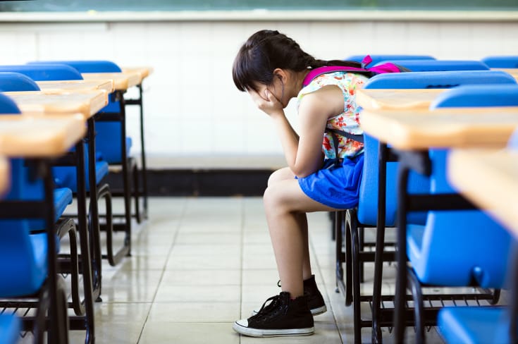 Una niña entierra la cara en las palmas de las manos y se sienta sola en clase: efecto perjudicial del estilo de crianza autoritario
