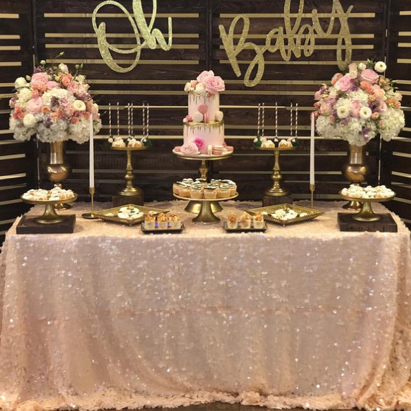 bebé con un motivo vintage con una mesa rosa brillante con velas, grandes ramos de flores, pasteles y otros postres