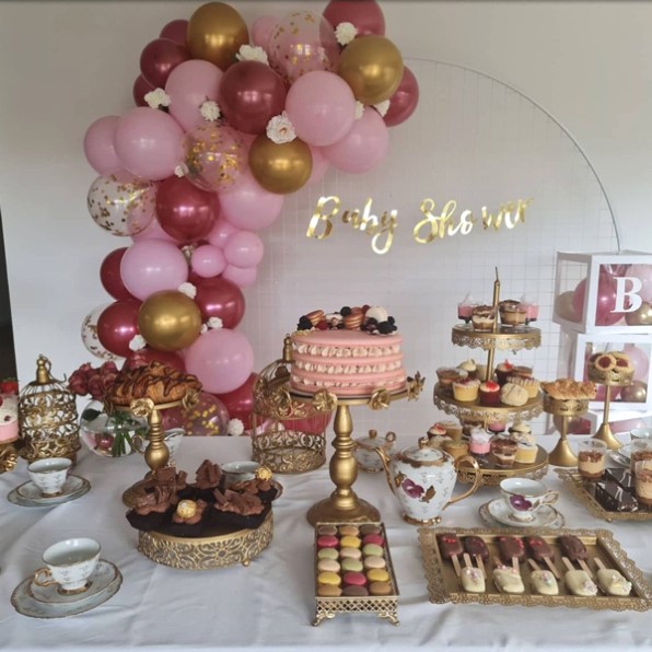 ducha para niños con merienda inglesa con globos rosados ​​y dorados y una mesa llena de dulces