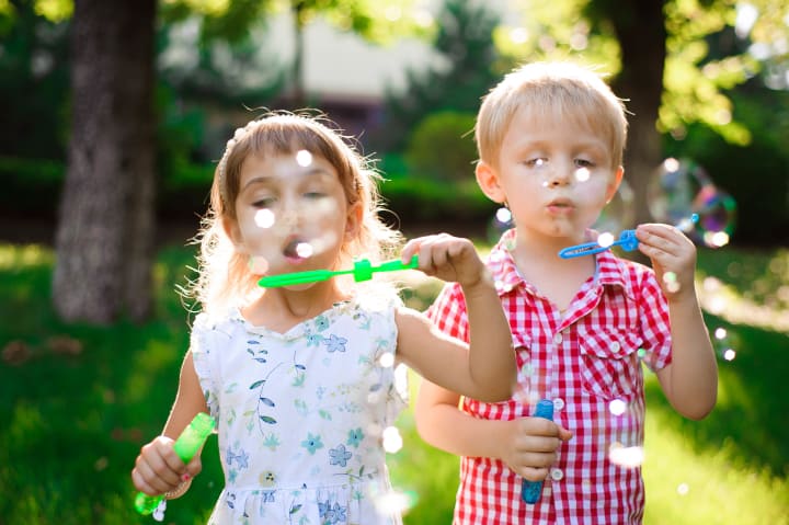 un niño y una niña soplando burbujas en el parque - la importancia del juego