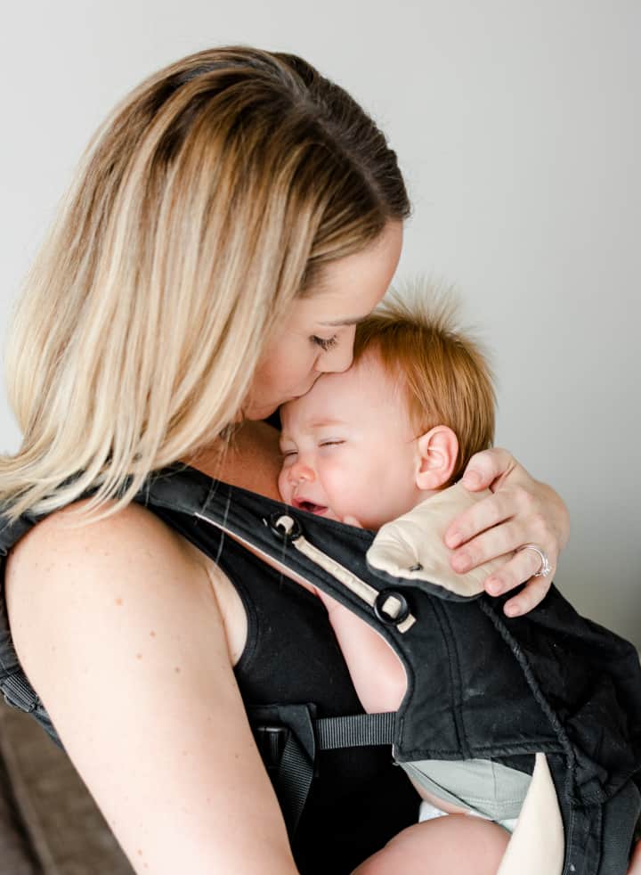 Una mujer lleva a su bebé dormido en un portabebés: qué es la crianza con apego y su efecto en el desarrollo del cerebro